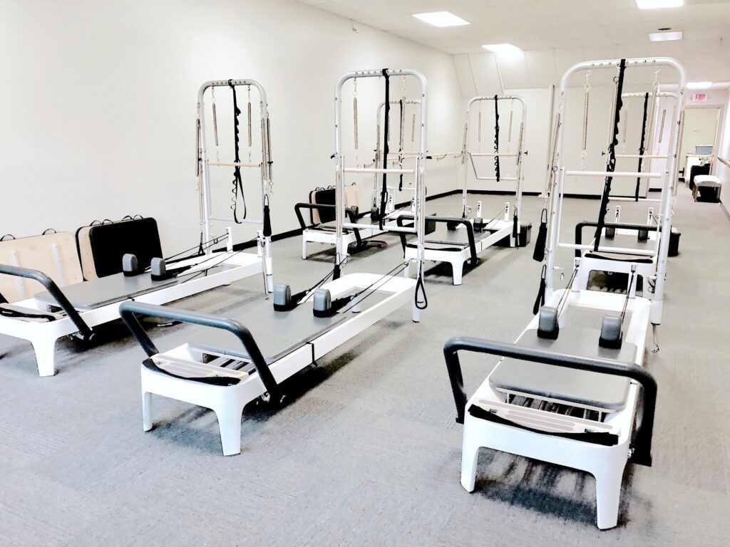 Pilates reformers in an empty exercise studio. - Pilates by Katie Pilates reformers in an empty exercise studio.